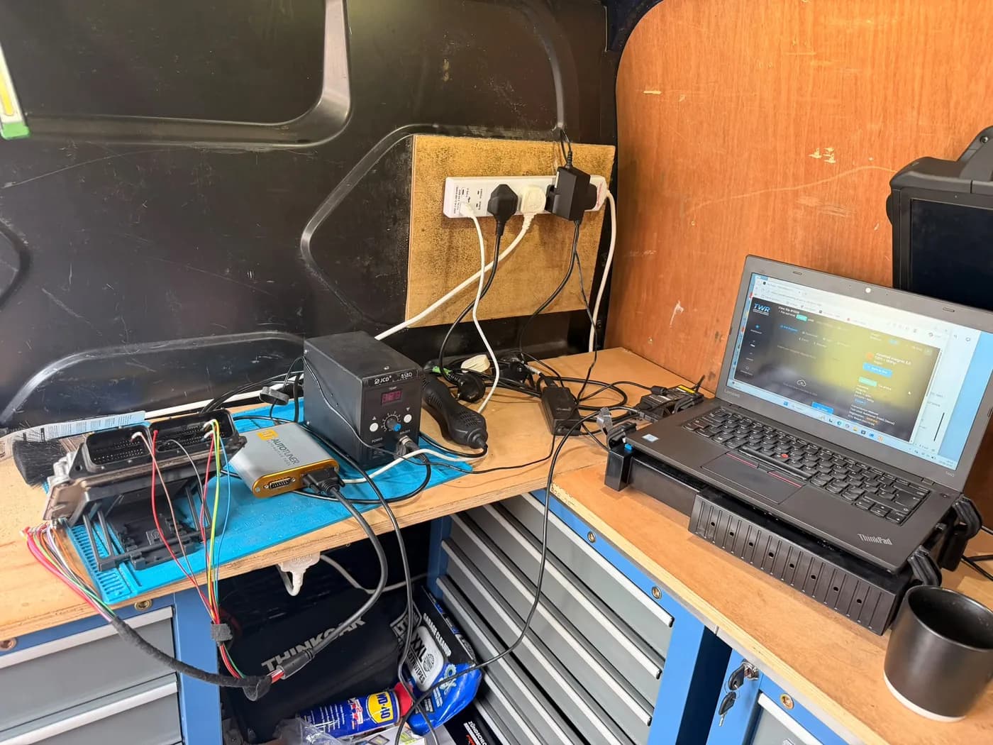 An engine ECU opened on the bench inside the Chester Tuning van, wired to the laptop so its software can be read