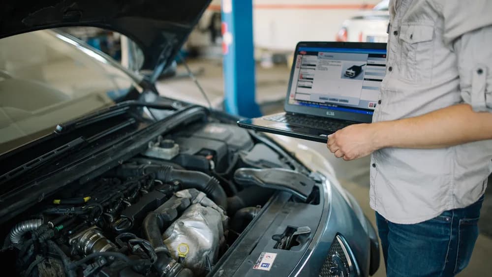A mechanic reading a car's ECU with a diagnostic laptop over the open engine bay